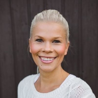 Nainen hymyilee kameralle tumma puutausta takanaan