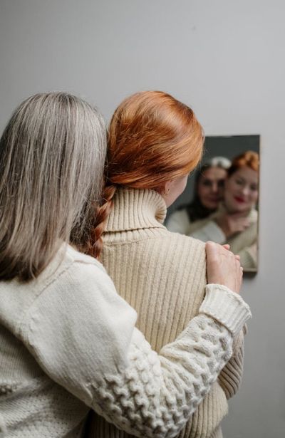 Kaksi naista halaa toisiaan katsoen peiliin